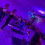 Children and instructors participating in a BUILD movement-based leadership fitness class under vibrant purple lighting at the Greek School of Plato in Brooklyn.