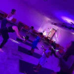 Children and instructors participating in a BUILD movement-based leadership fitness class under vibrant purple lighting at the Greek School of Plato in Brooklyn.