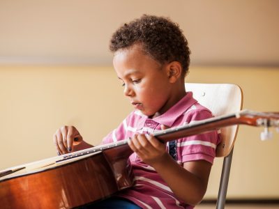 Side view of boy playing guitar while sitting on chair